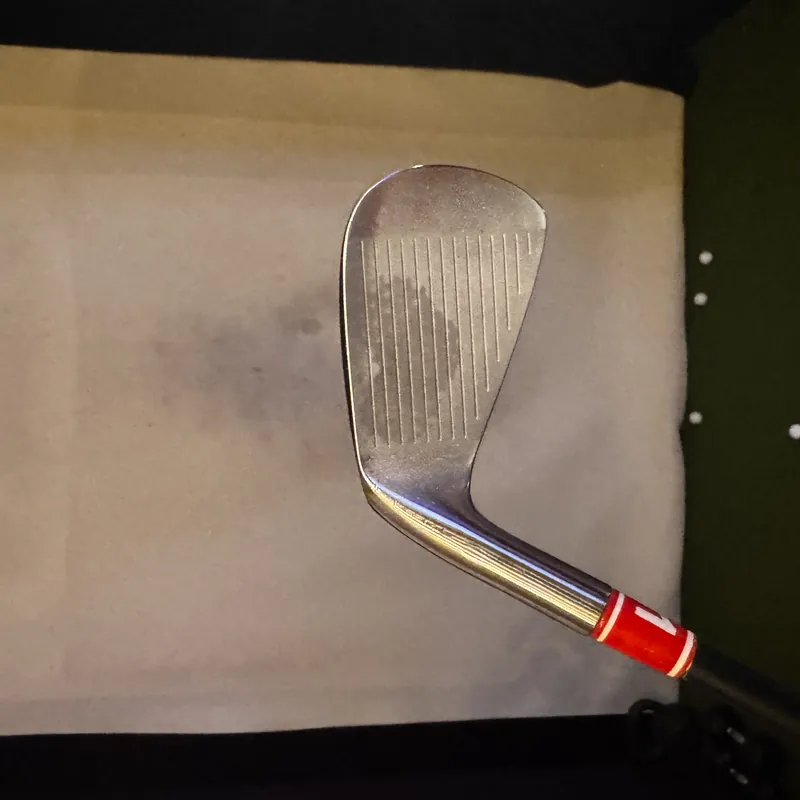 Seven-iron with a red tape band on the shaft, at address against an impact screen